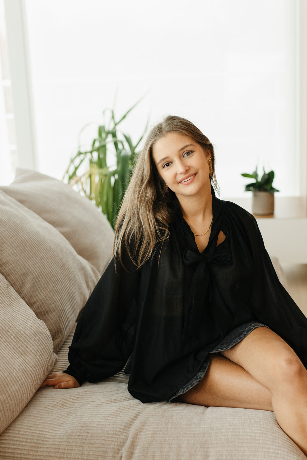 Model draagt zwarte transparante blouse met strik aan de hals