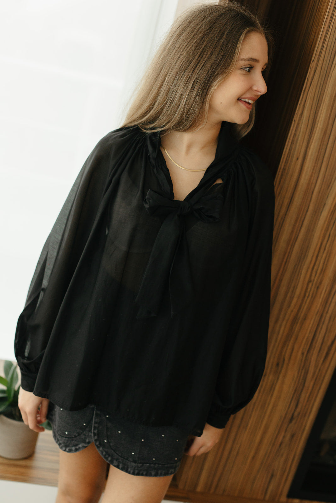 Model draagt zwarte transparante blouse met strik aan de hals