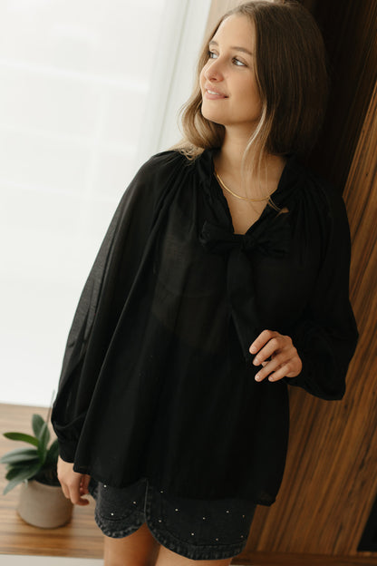 Model draagt zwarte transparante blouse met strik aan de hals